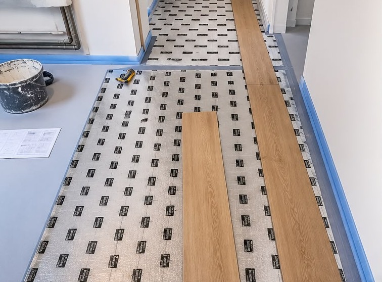 Pose d'un sol aspect bois en cours sur sous-couche dans un couloir – DFE RENOV